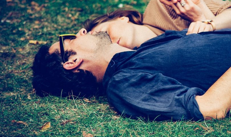 Man and women sleeping next to each other on grass.