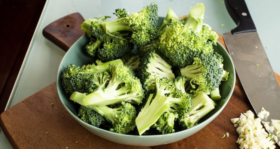 A small bowl of chopped broccoli on top of a wooden cutting board