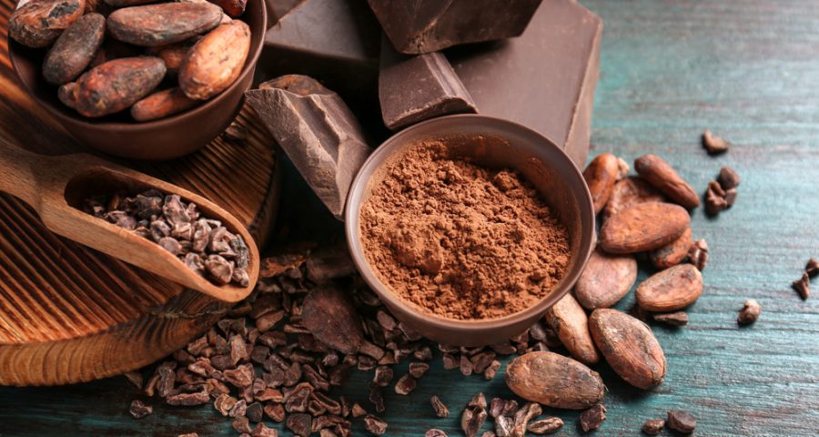 Bowls of cocoa beans and powder with broken chocolate pieces on color background from depositphotos.com